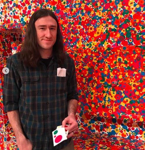 Daniel Bailey against a colorful dotted background at Kusama's Infinity Mirrors art exhibit.